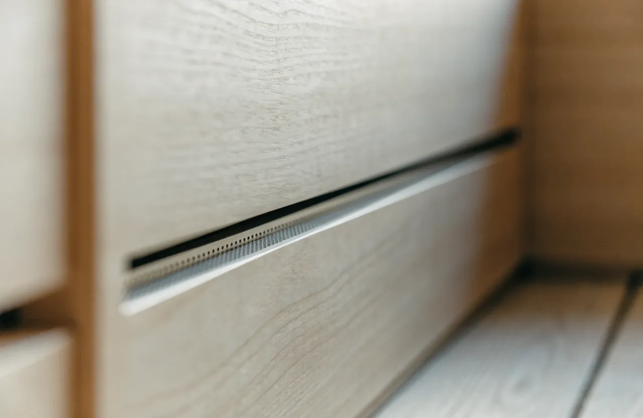 A narrow ventilation slot set low in a pale timber wall