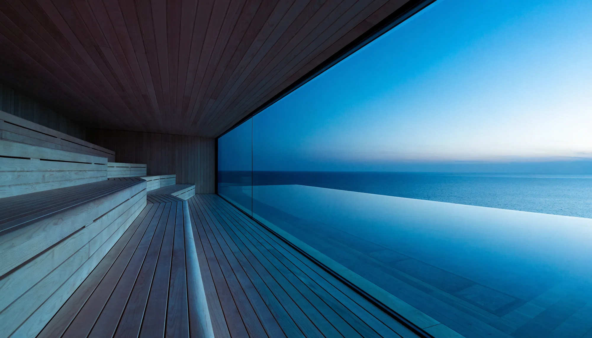 A sauna with a full-height glass wall looking over an infinity pool to the ocean